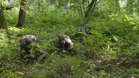 Soldiers in Camouflage with Rifles Crawling Across Thicket in Forest