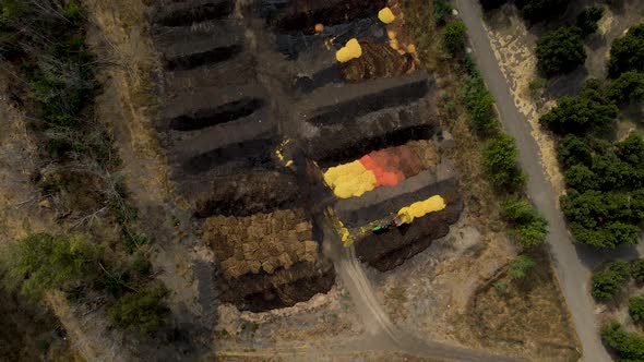 Aerial top down dolly in of a tractor discarding orange shells in a compost area surrounded by plant