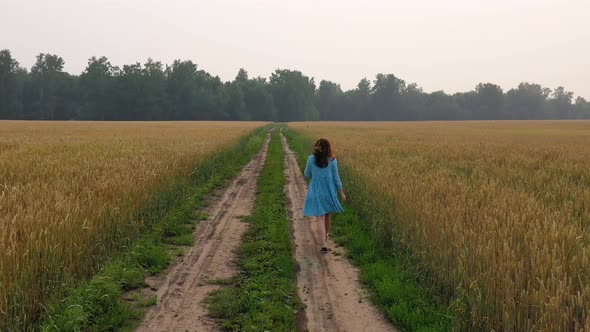 A Young Girl in a Dress Walks Along a Wheat Field