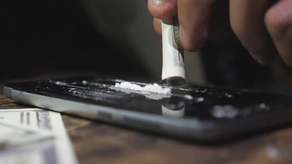 Male Addict Sniffing Cocaine Line From Phone Screen Through Twisted Dollar Bill