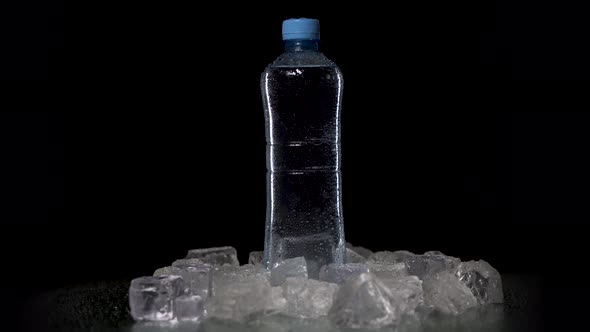 Transparent Bottle with Fresh Pure Mineral Water Spin on Table. Bottle Stands on Black Table