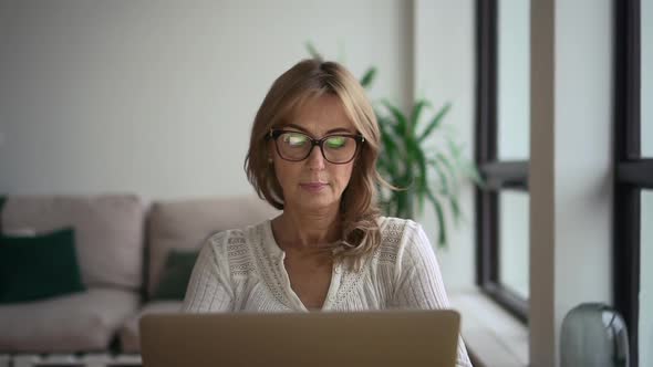 Front View of Businesswoman Working with Laptop and Sitting at Table in Modern Home Office