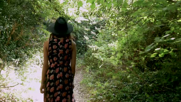 Young woman walks down a narrow path through a dense wood.