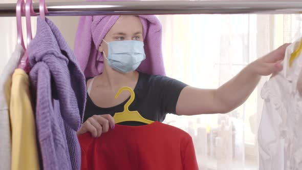 Young Woman in Hair Towel and Face Mask Taking Hangers From Garment Rack and Leaving