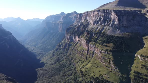 Smooth aerial footage of a huge and green chain of mountains at sunrise.