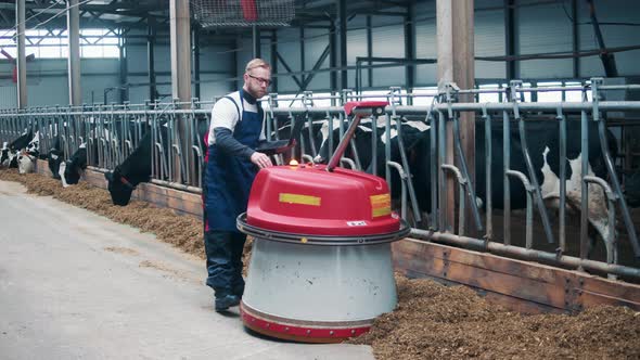 Male Worker is Operating a Robotic Feed Pusher in a Cowshed