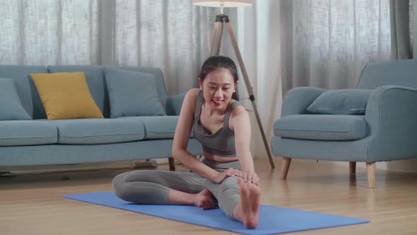 Asian Athletic Female In Sports Clothes Sitting On A Yoga Mat And Doing Hamstring Stretch