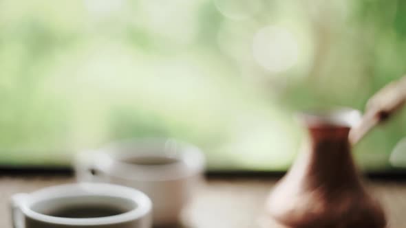 Coffee cups and cezve with Turkish coffee close to window with view on green trees close up slow mot