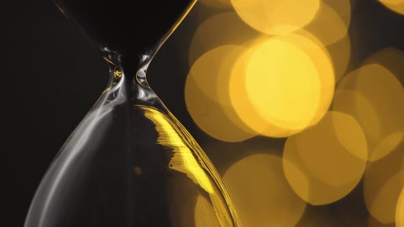 Sand Falling in Hourglass Against Golden Bokeh Background Close Up