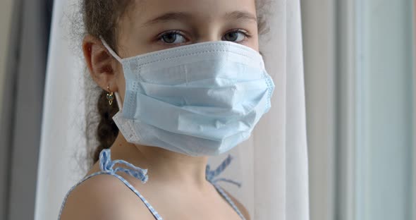 Portrait of a Cute Little Child or Little Girl in a Protective Medical Mask Looks Out the Window