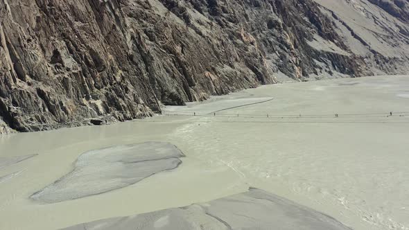 aerial drone overlooking a large gray river flowing between a large set of mountain cliffs in Hunza