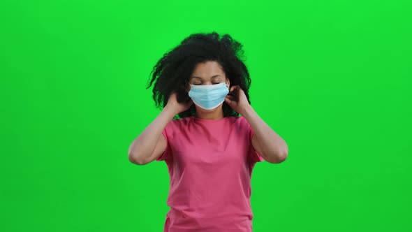 Portrait of Young Female African American Looking at the Camera and Puts on Medical Mask