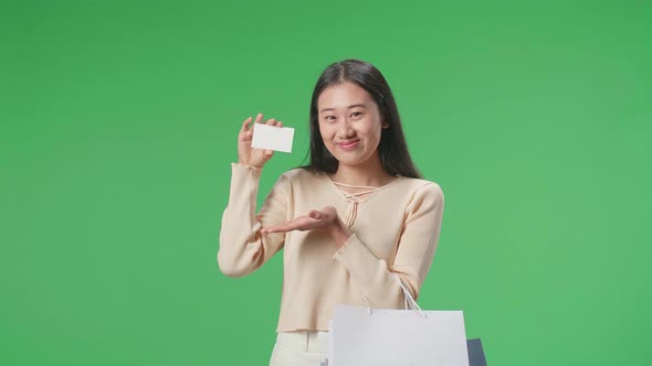 Asian Shopping Woman With A White Card And Shopping Bags Smile To Camera On Green Screen