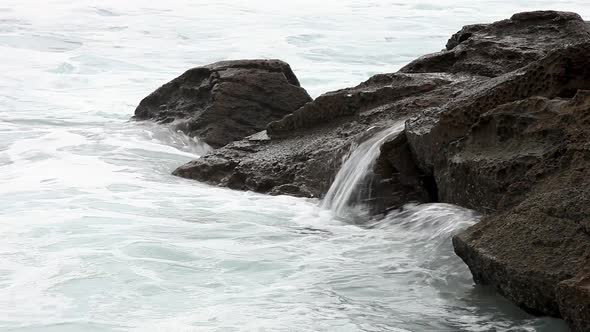 Miniature waterfalls created over seaside rock pools as they get smashed by the rolling waves.