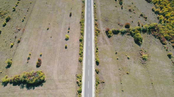 Top Aerial View of an Empty Asphalt Road on the Plateau Between Green Fields