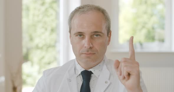 Close-up Portrait of Confident Serious Doctor Sitting with Raised Finger and Looking at Camera