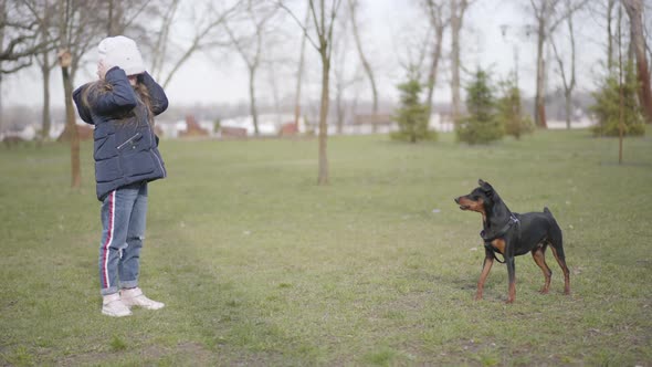 Little Caucasian Girl Kicking Away Barking Dog in Park. Wide Shot of Frightened Kid and Angry