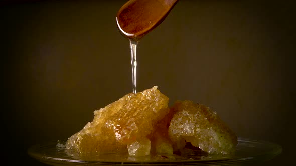 Honey Flows From a Wooden Spoon on a Honeycomb