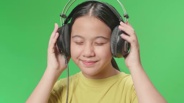 Young Asian Kid Girl Listening To Music With Headphones And Dancing In The Green Screen Studio