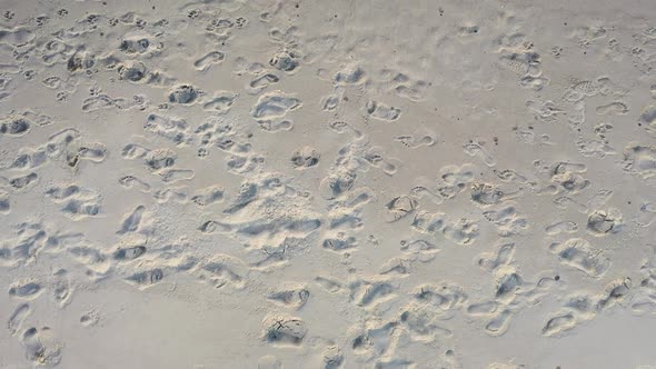 AERIAL: Ascending Shot of Human Footprints in the Sand on a Beach