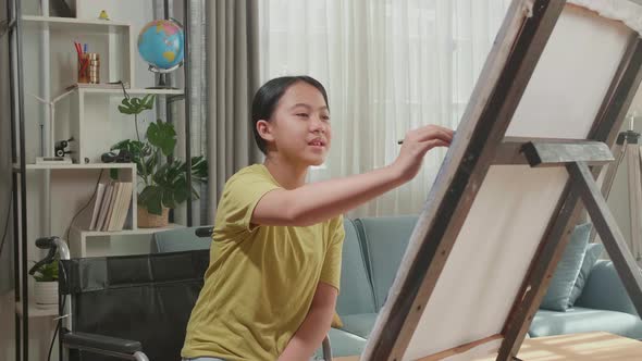 Asian Artist Girl In Wheelchair Holding Paintbrush Thinking And Painting On The Canvas