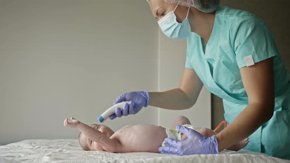 Pediatrician Measures the Temperature of the Newborn with a Non-contact Thermometer in the Clinic