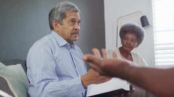 Mixed race senior male counsellor with clipboard advising to group of diverse senior friends