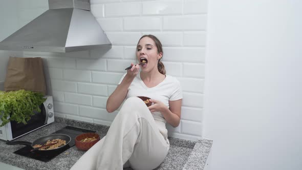 Carefree Woman Eating While Sitting On Kitchen Countertop