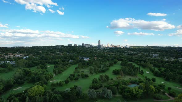 green golf course with skyline of Sandton in Johannesburg during day, aerial