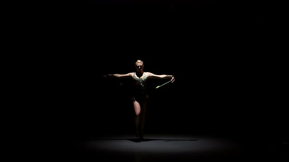 Girl Gymnast Doing Acrobatic Movement with a Mace in His Hand. Black Background