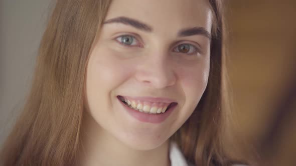 Close-up Portrait of Beautiful Young Smiling Woman with Different Colored Eyes Looking at Camera