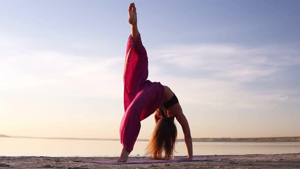 Close Up View of a Young Woman in Pink Yogi Pants Practicing on Sand Near the Sea or Lake in the