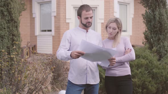 Young Caucasian Male Designer Showing His Client Blueprints and Explaining Drawings