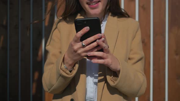 Hands of Young Woman Holding Smartphone Outdoors in Sunny Weather