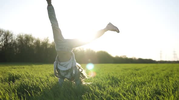 Front View of a Beautiful Young Girl Doing Somersault Outside on the Green Field