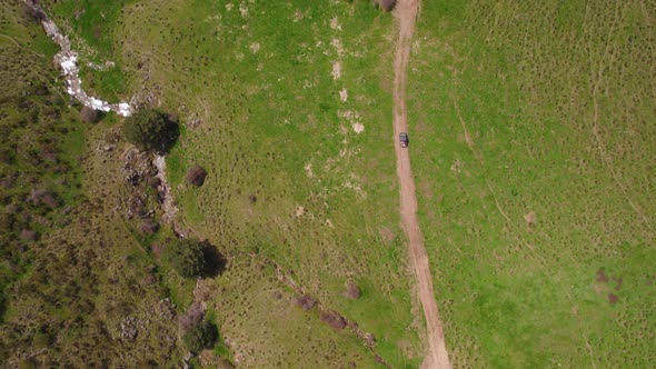 Aerial top down shot of 4x4 car driving on rural path between green fields during sunlight