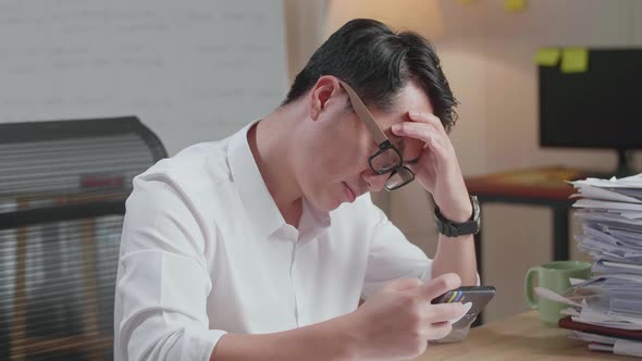 Close Up Of Asian Man Being Upset Losing Game On Smartphone After Working With Documents