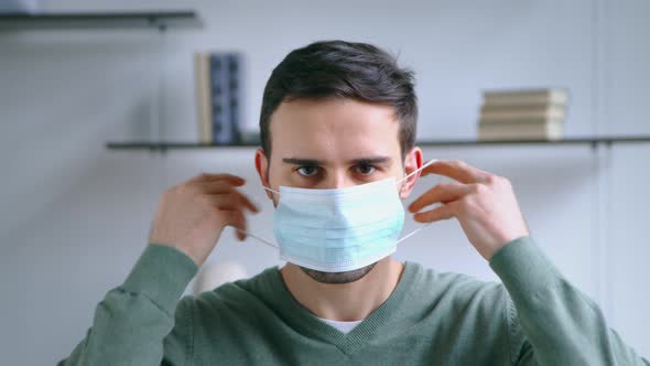 A young man puts on a blue medical mask. Young guy putting on a mask