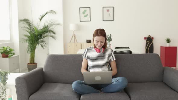 Young Woman Using Laptop Computer Sitting on Sofa at Home alt