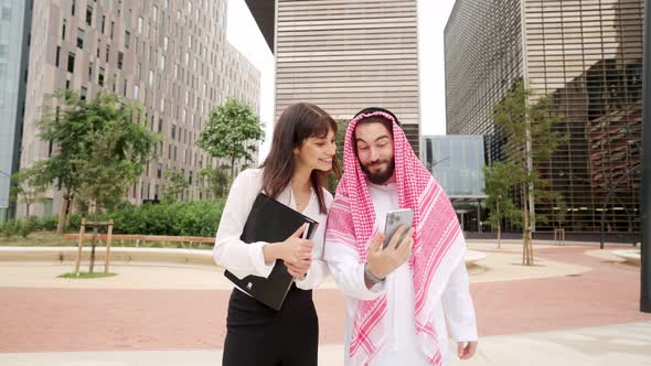 Cheerful Arab Man Showing Cellphone to Businesswoman