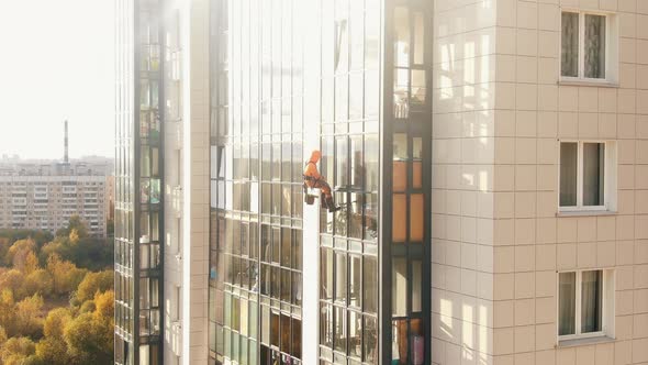 Laborer in Orange Suit Washes Windows of Apartment Building