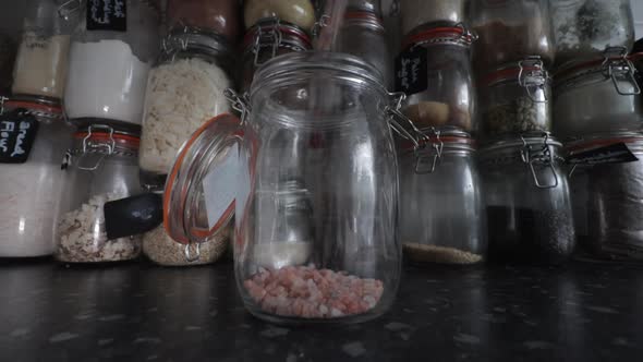 Himalayan rose pink salt pouring into Kilner clip top jar infant of wall of ingredients.