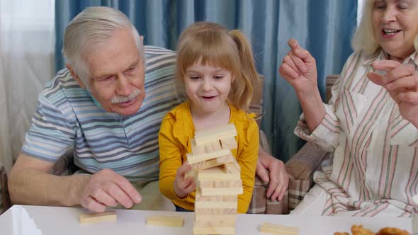 Excited Child Girl Kid Involved in Build Blocks Board Game with Senior Grandmother and Grandfather