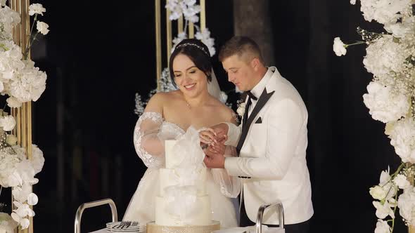 Newlyweds Cut the Wedding Cake Lovely Bride and Groom Couple Cutting Dessert with a Knife Outdoors