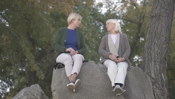 Elder Mother and Middle Aged Daughter Sitting on Stones and Talking About Life