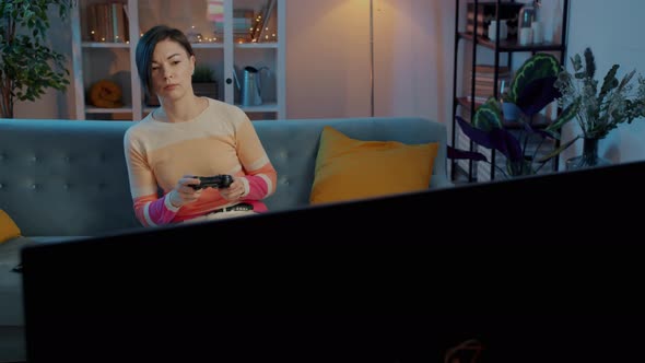 Carefree Woman Playing Video Game Relaxing on Comfortable Couch Indoors in the Evening