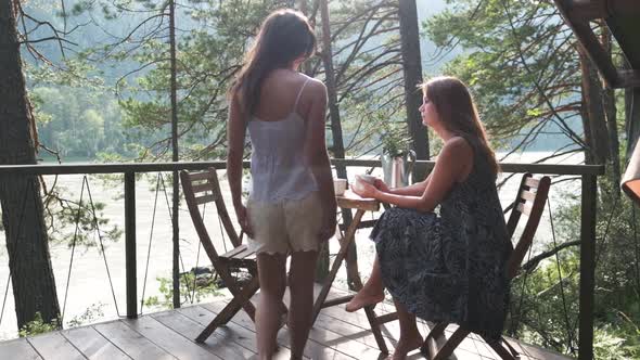 Two Attractive Girls Are Sitting at a Coffee Table on the Balcony, Enjoying Nature. Two Girlfriends