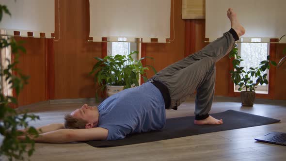 Fit Caucasian Man Doing Yoga Exercise Stretching Leg Muscles and Abs Using Computer at Home