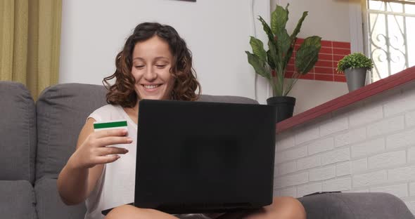 Happy young woman shopping with her credit card and laptop on the couch at home