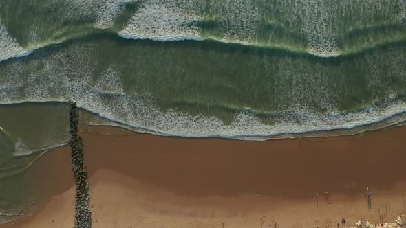 Brown Beach and Green Ocean with Rock Wall Formation and Few Surfers and People at Sunset